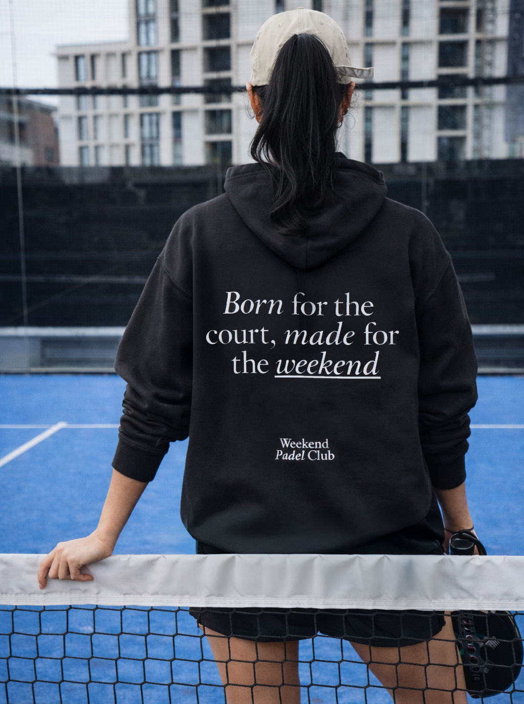 Person wearing a black hoodie with text on a PADEL court